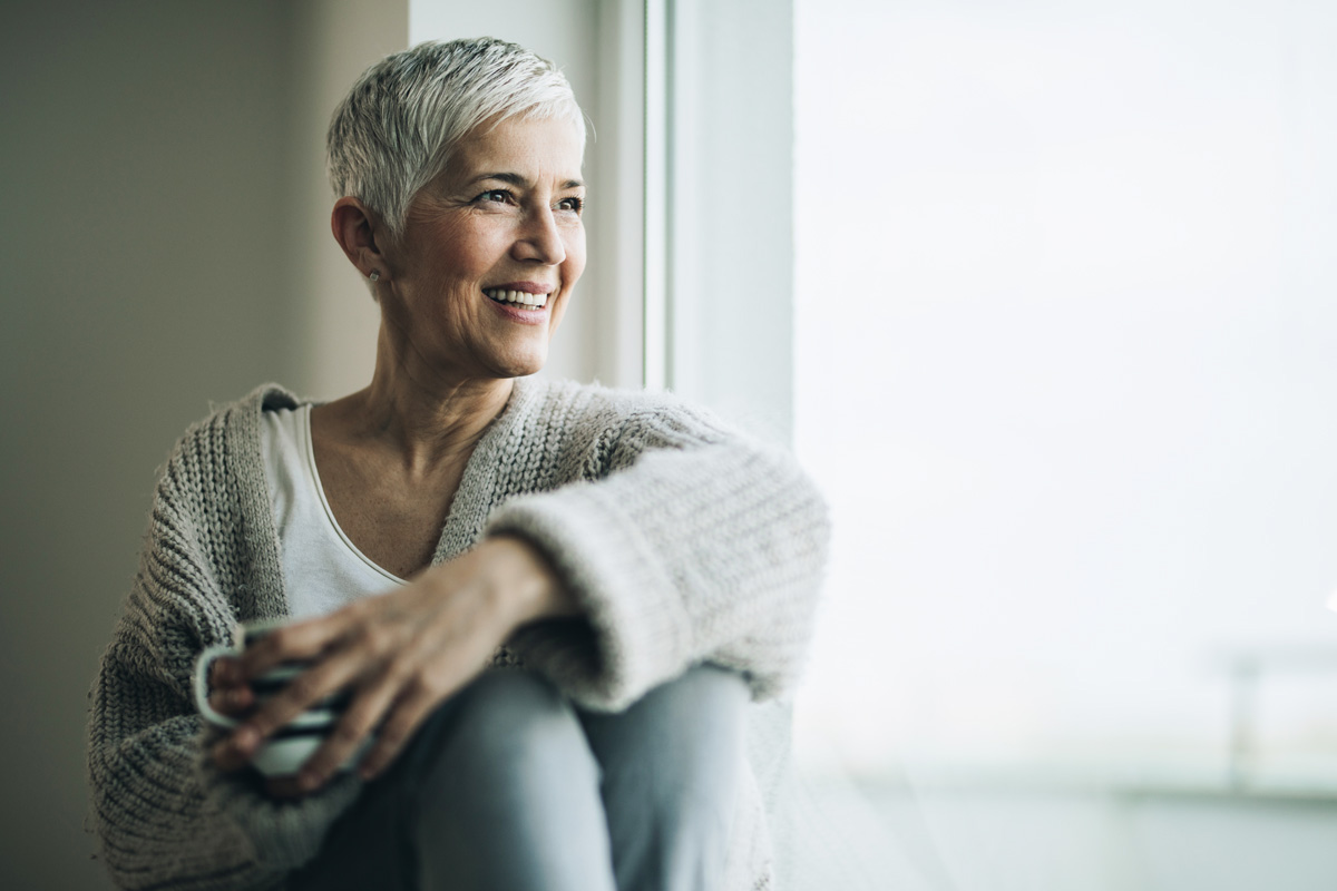 Happy senior woman relaxing by the window during coffee time. Copy space.