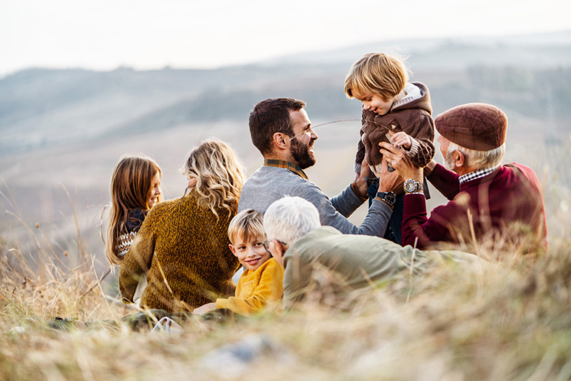 Happy extended family enjoying while relaxing during autumn day on the field. Copy space.