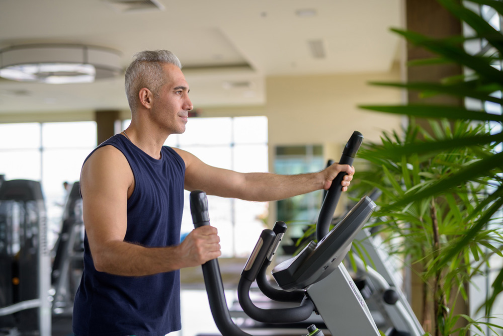 Portrait of mature handsome Persian man with gray hair exercising at the gym