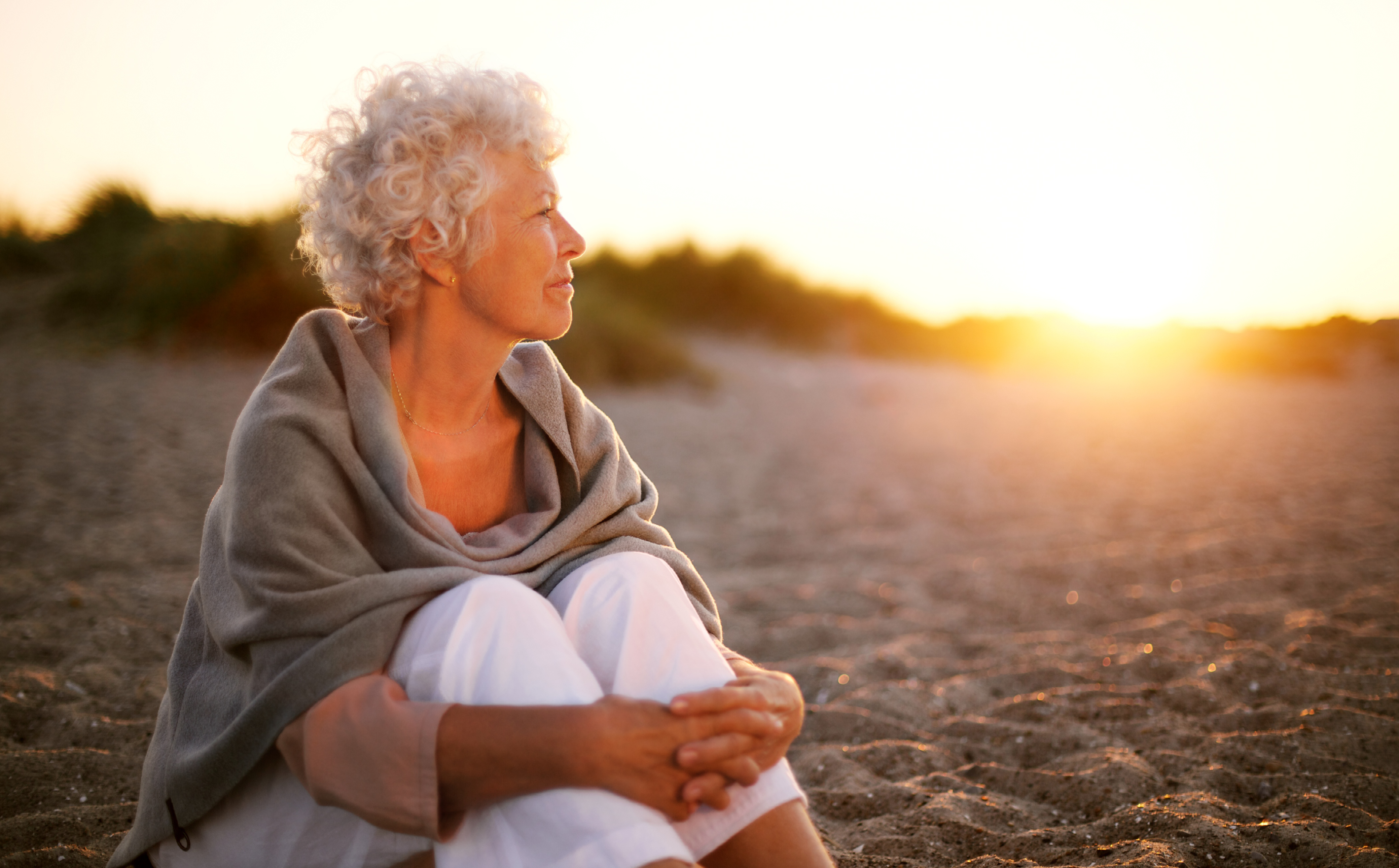 Older woman sitting on beach at sunset