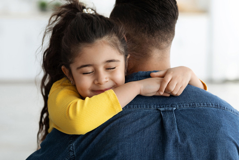 Father's Day Concept. Cute Little Arab Girl Hugging Tight Her Dad At Home, Loving Small Female Child Embracing Daddy With Closed Eyes, Happy Middle Eastern Family Bonding Together In Kitchen, Closeup