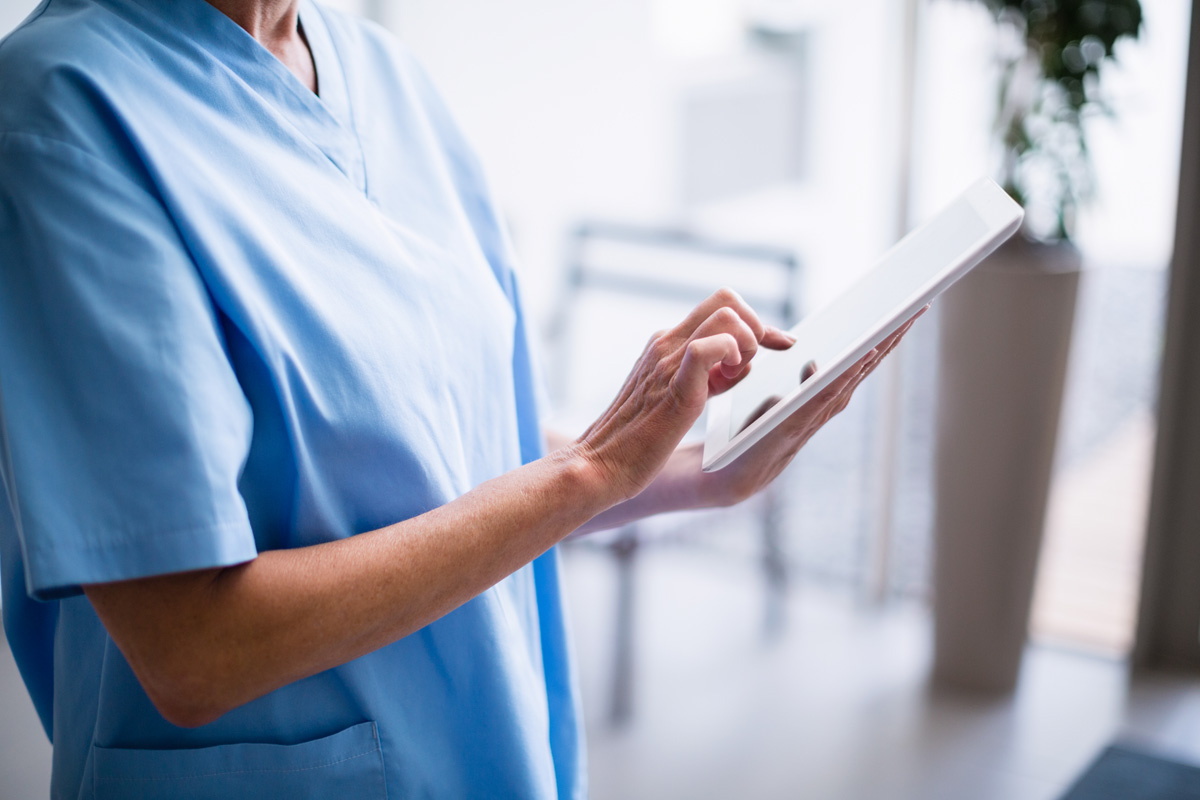 Mid section of nurse standing in hospital corridor using digital tablet