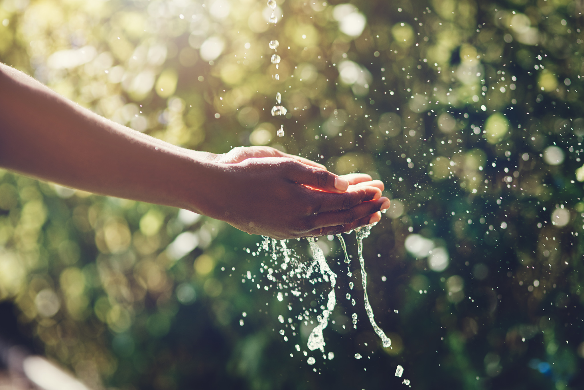 Closeup shot of a man holding his hands under a stream of water outdoors