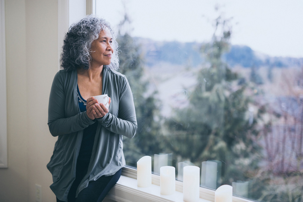 Mature and vibrant Hawaiian woman stands by her window in the early morning and contemplates the mysteries of the universe.