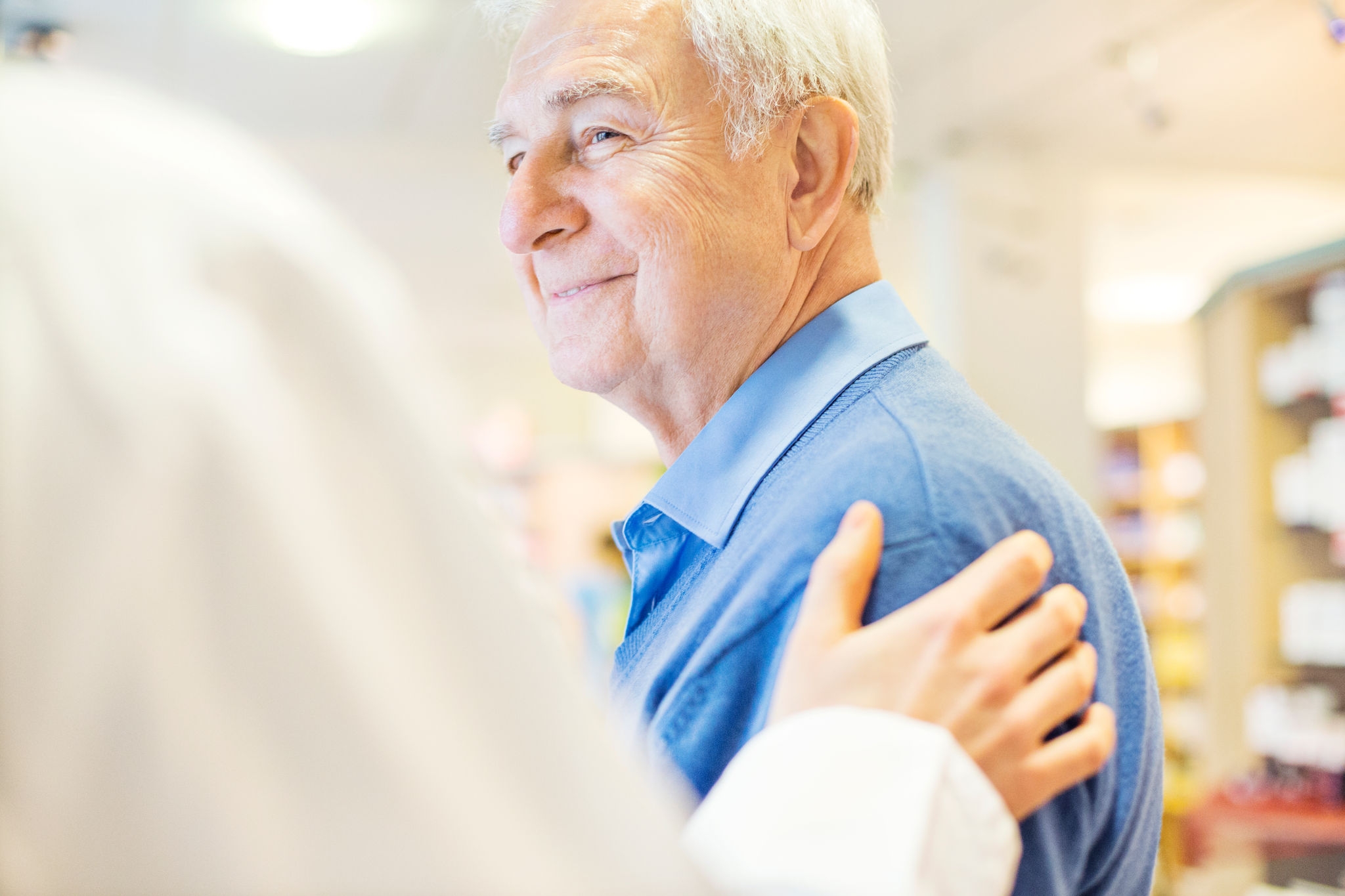 669896492 Cropped image of female pharmacist consoling senior man in store. Smiling male customer is looking at chemist. They are at brightly lit pharmacy.
