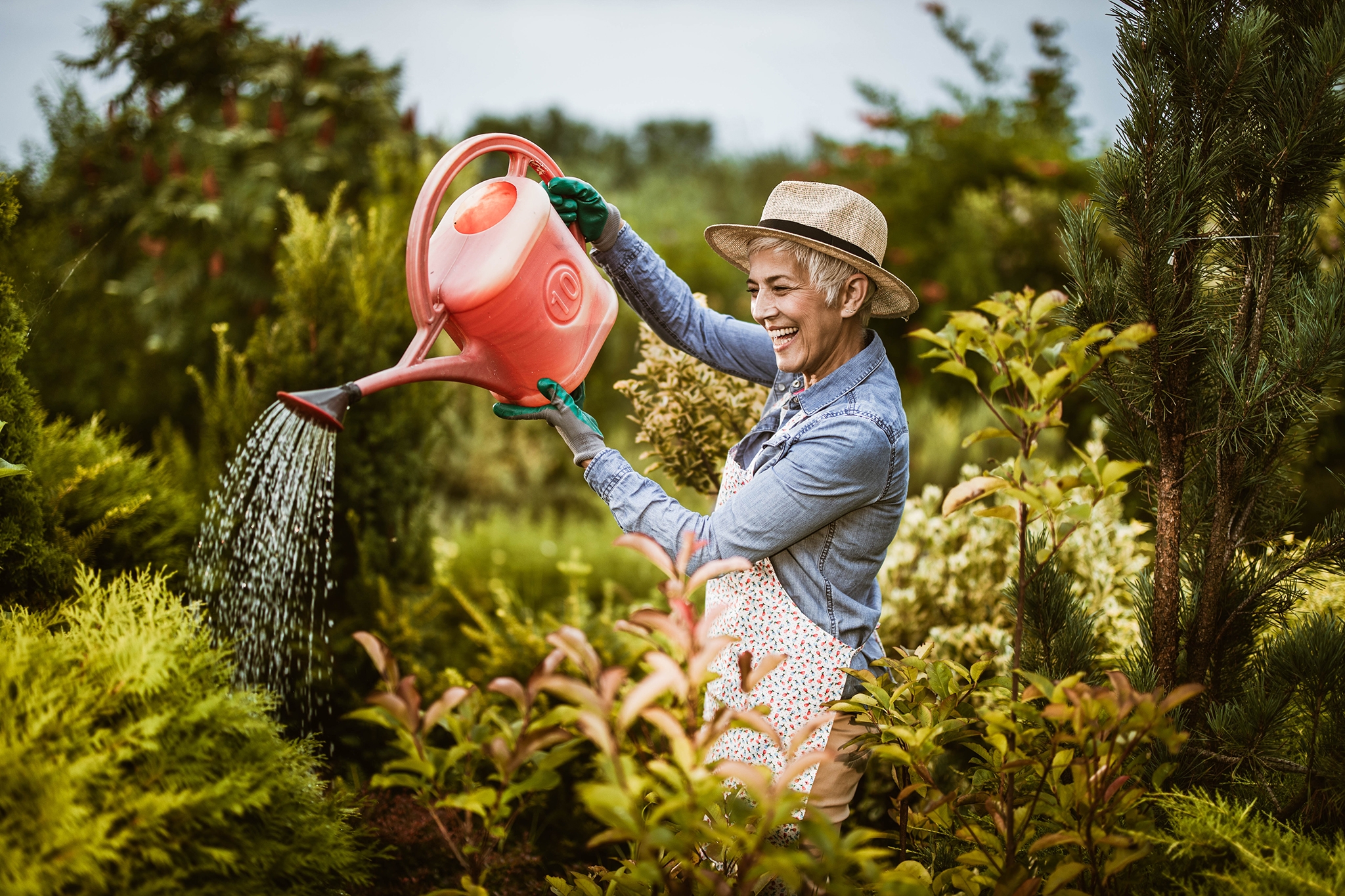 Happy mature woman watering her plants in the backyard.