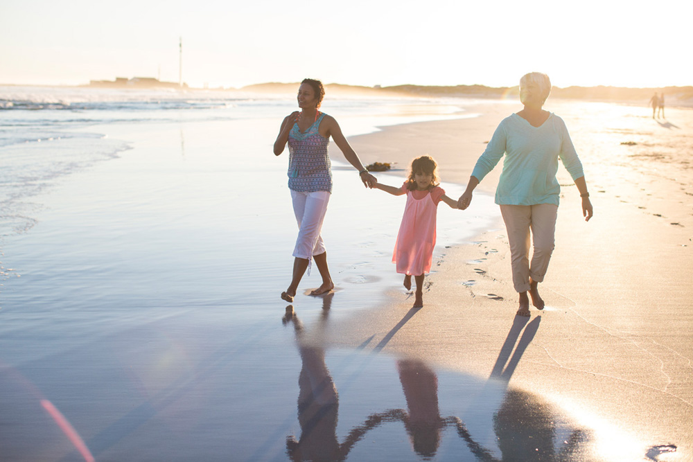 Grandmother, her daughter and her grand daughter walking along together on the beach at sunset