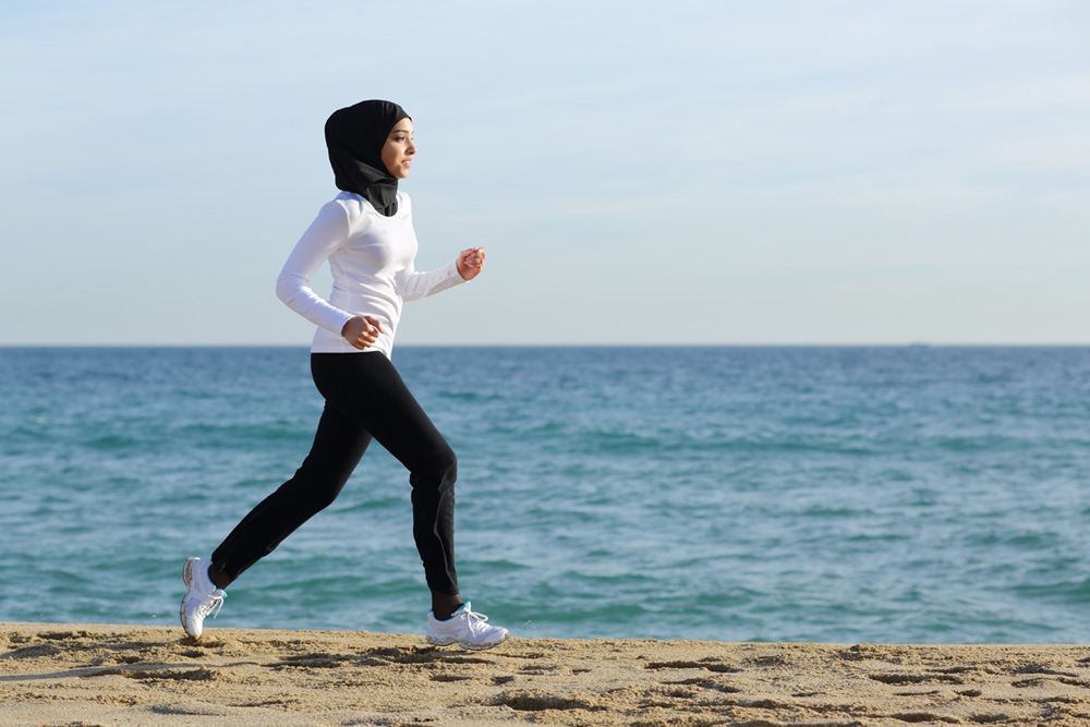 Arab saudi runner woman running on the beach with the sea and horizon in the background