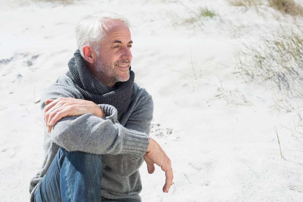 Attractive man smiling on the beach in scarf on a bright but cool day