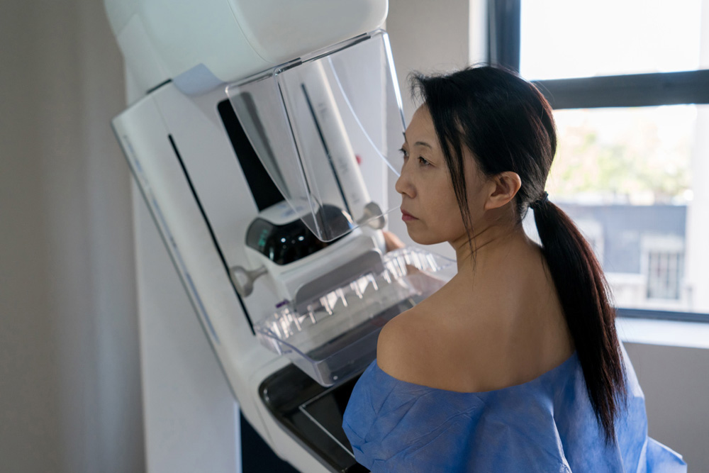 Asian female patient at the hospital getting a mammogram exam using a hospital gown and looking very serious