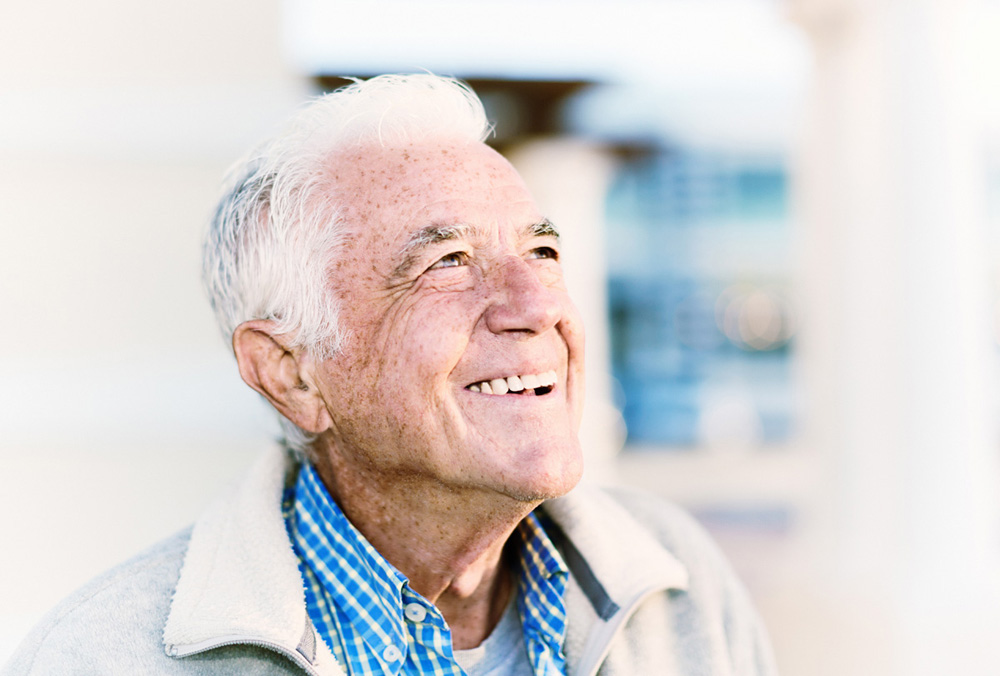 A relaxed senior man smiles, standing outdoors and looking up in the winter sunshine.