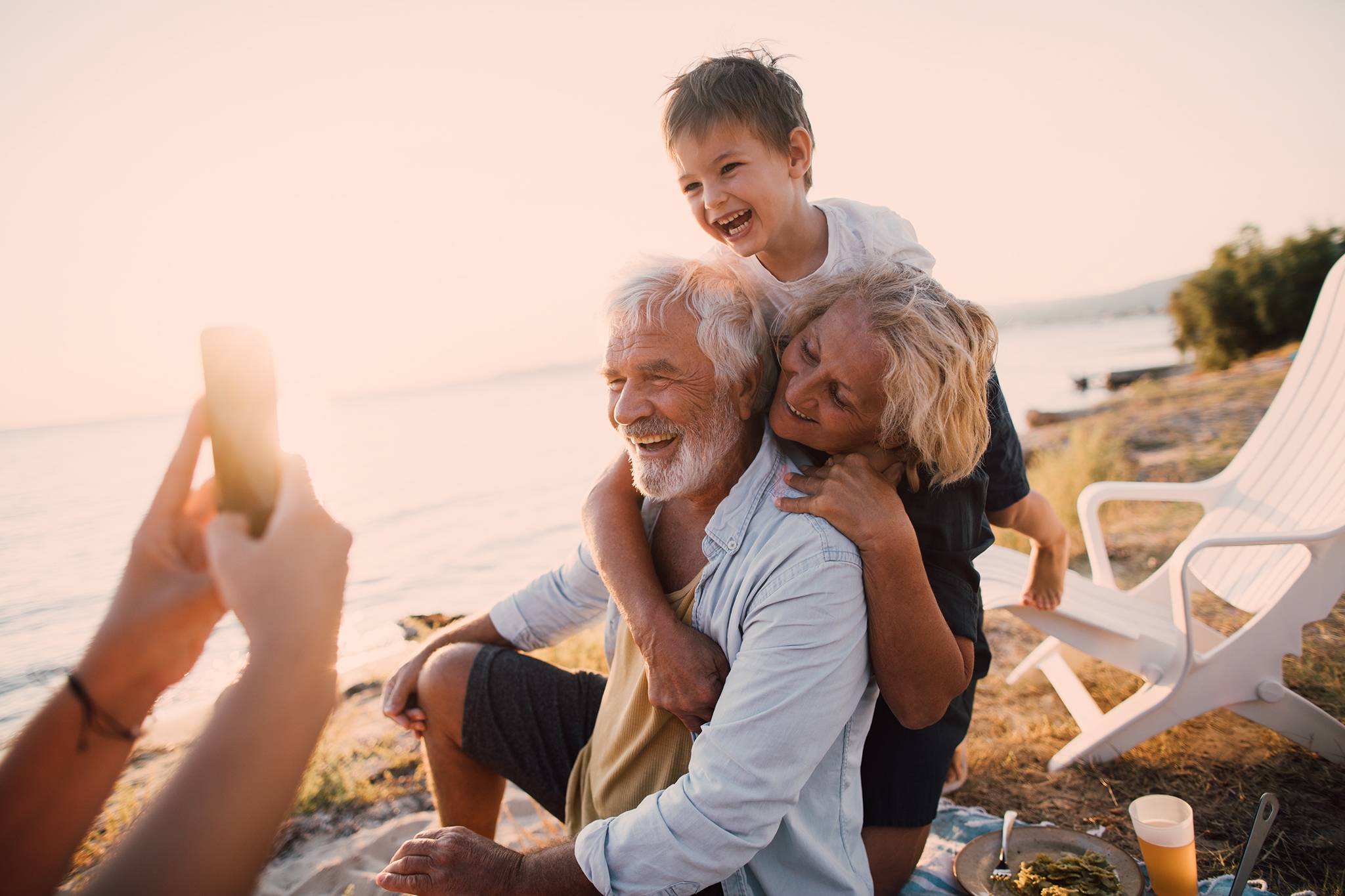 Photo of a multi-generation family having a picnic by the seaside, taking photos with a mobile phone to capture precious moments