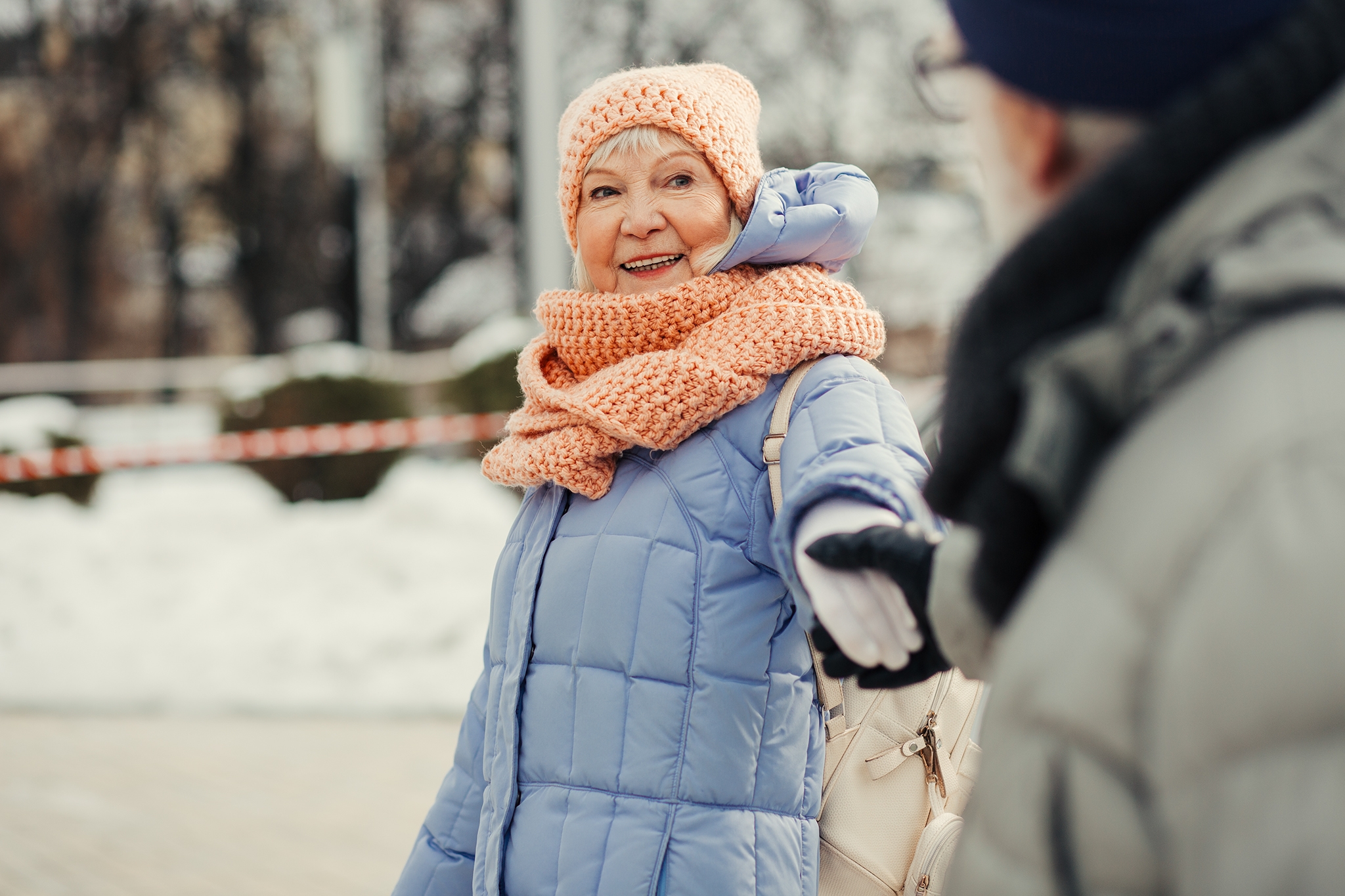 Cheerful aged woman in winter clothes walking with her husband and smiling while holding his hand