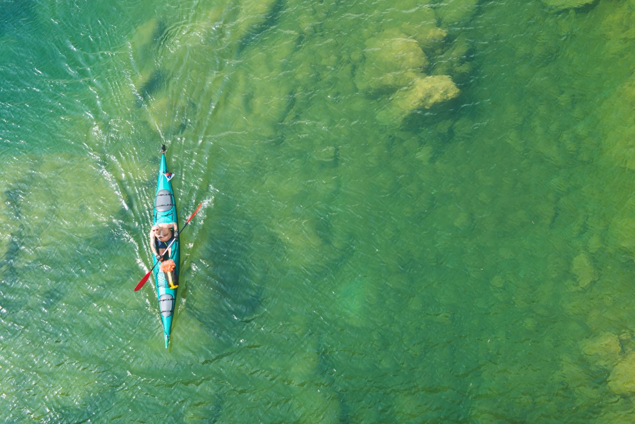 hombre en kayak sobre lago color verde vista zenital